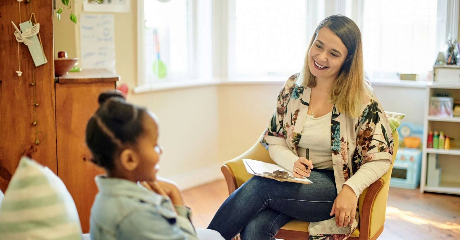 A psychologist sits with a notepad, smiling warmly at a child.