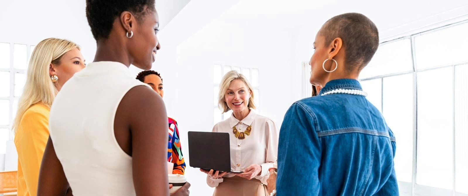 A group of five women in a bright office engage in a friendly discussion.