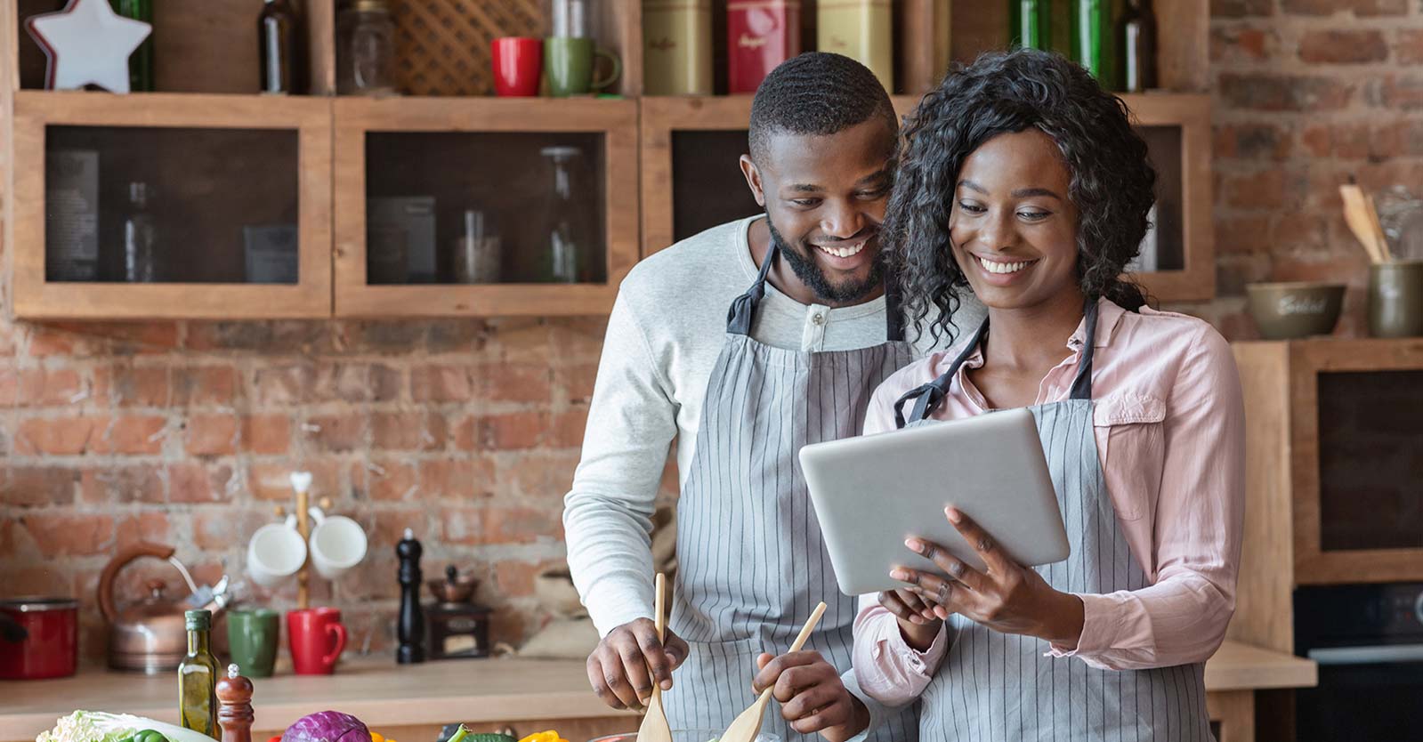 Two people preparing a meal in a kitchen and reading a tablet.