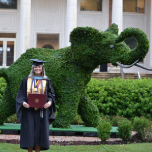 Hannah Jackson holding degree in front of elephant shaped bush