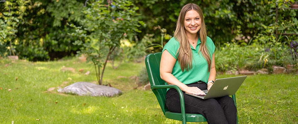 Student holding a laptop while sitting outside